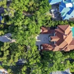 Aerial view of a Sarasota home with lush tropical landscaping, palms, pool, and waterfront